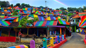 Un vivace paesino con case dipinte in vari colori vivaci, tra cui rosso, giallo, blu e verde, con un arcobaleno nel cielo e recinzioni multicolori che costeggiano la strada.